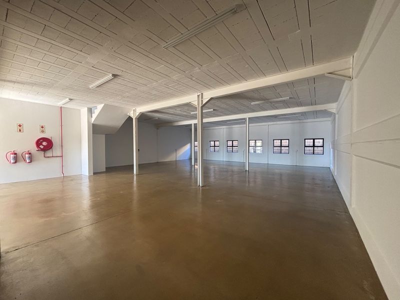 A spacious, open-plan industrial utility area featuring polished concrete floors, exposed beam ceilings, and steel support columns, suitable for various commercial or storage uses.