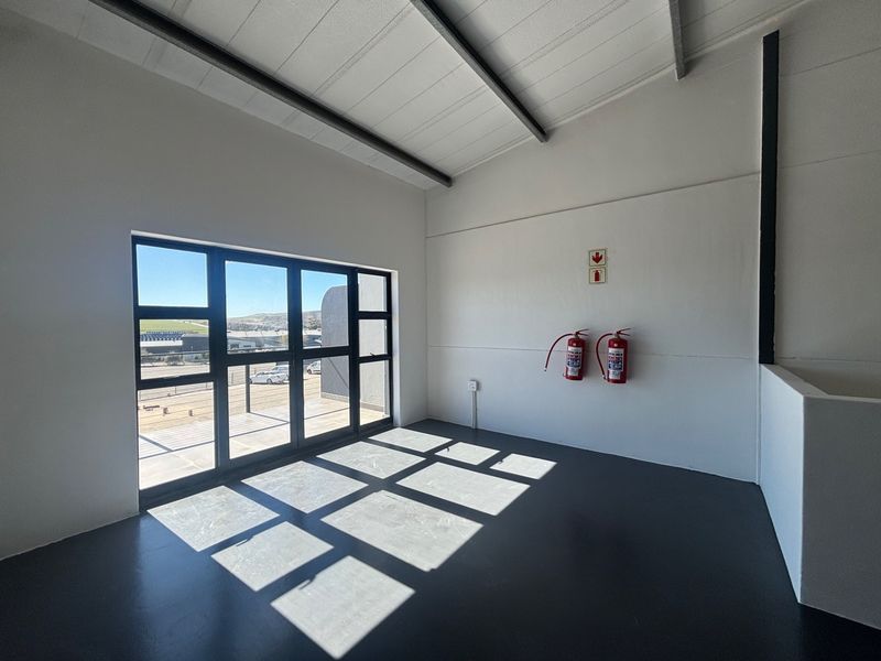 A bright, modern industrial office space featuring clean white walls, durable epoxy flooring, and large windows providing ample natural light.