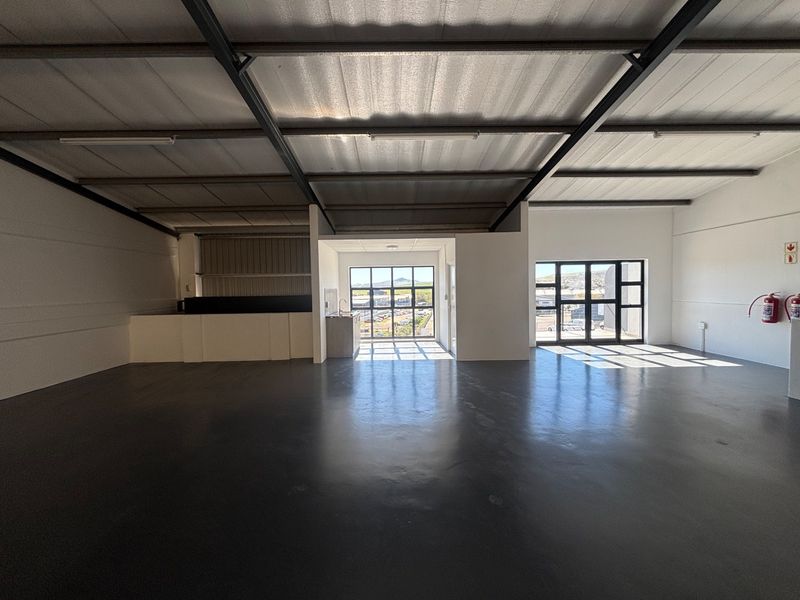Spacious open-plan industrial unit featuring high ceilings with exposed steel trusses, polished concrete flooring, and large windows providing ample natural light.