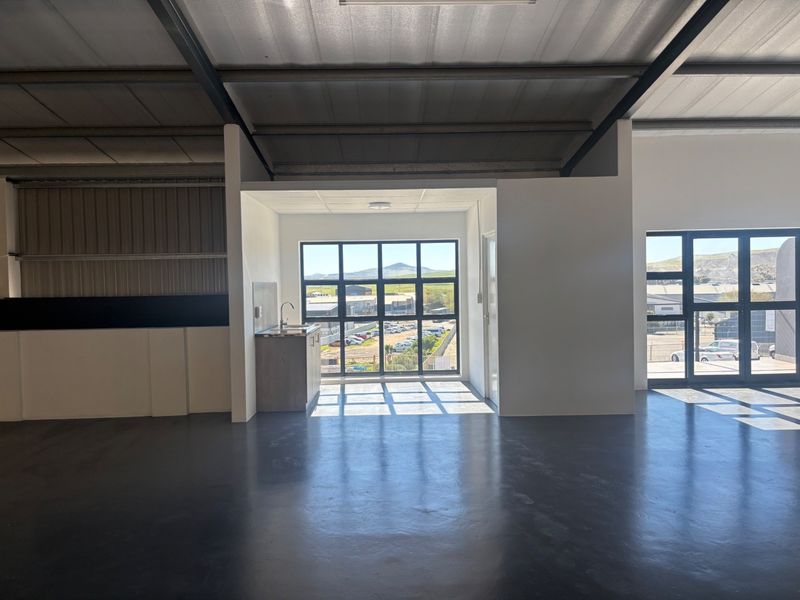 Spacious industrial open-plan area featuring polished epoxy flooring, exposed steel roof structure, large aluminum windows, and a compact kitchenette unit.
