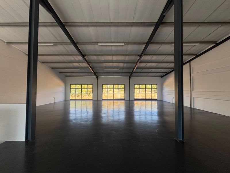 Spacious industrial warehouse unit featuring a clean epoxy-coated concrete floor, exposed steel portal frame structure, and ample natural light through grid windows.