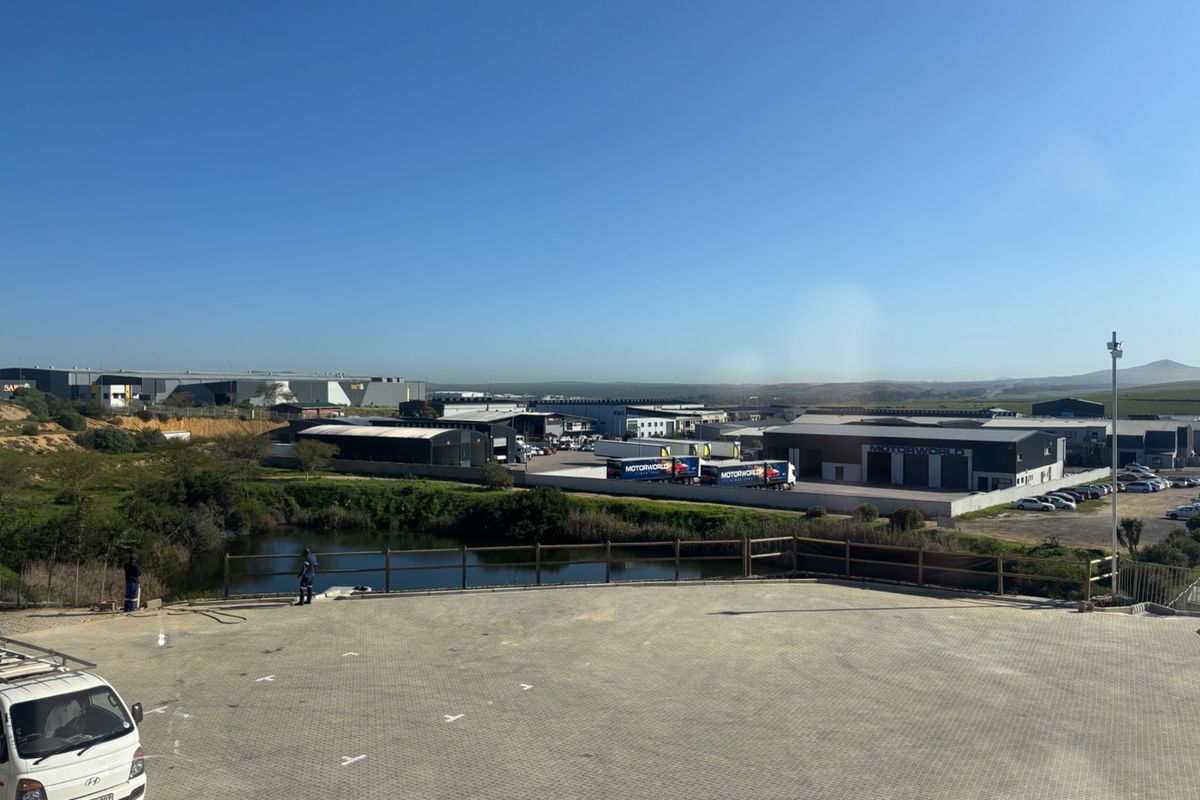 Elevated aerial view of an industrial property featuring a paved parking area, perimeter fencing, and surrounding commercial warehouse facilities.