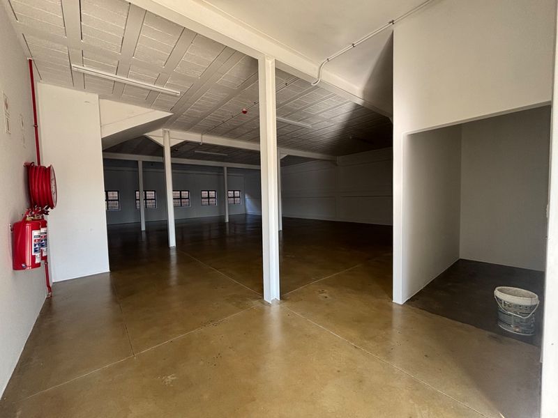 Spacious open-plan industrial warehouse area featuring polished concrete floors, exposed structural columns, and integrated fire safety equipment.