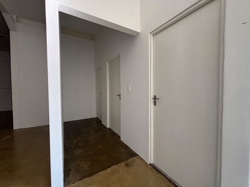 A clean, minimalist industrial hallway featuring smooth white walls and durable concrete flooring, providing access to multiple internal rooms.