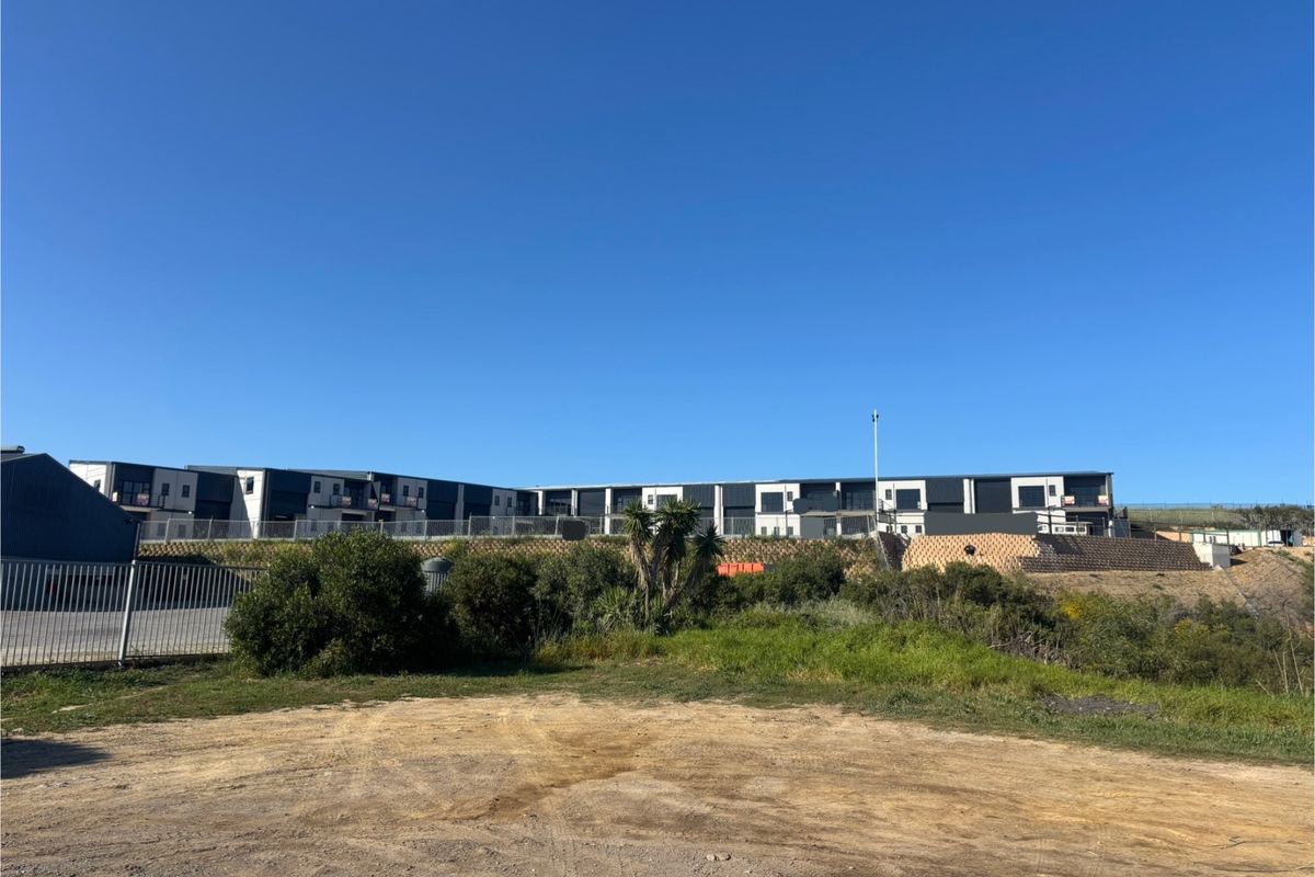 A wide-angle view of the rear elevation of a modern industrial-style multi-unit complex, featuring tiered retaining walls and landscaped grounds.