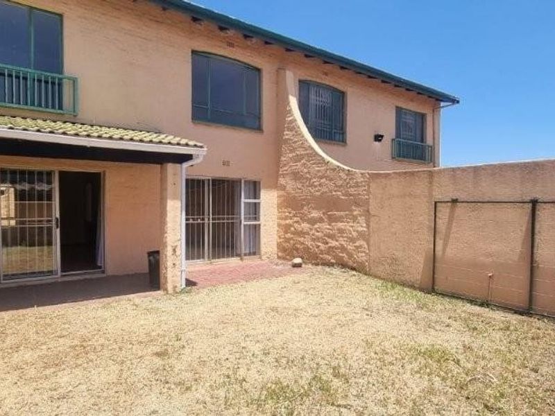 Rear view of the townhouse featuring a private garden, paved patio area, and sliding glass doors leading into the living space.