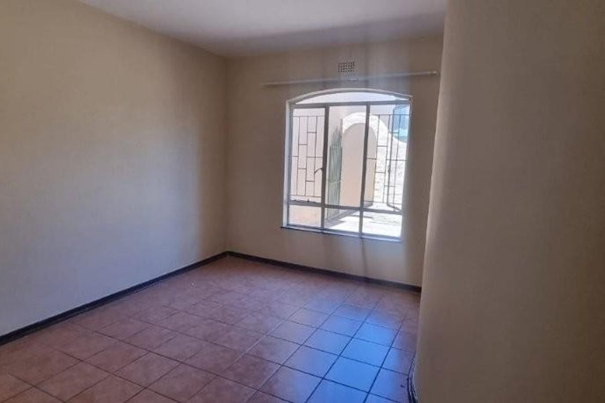 A vacant bedroom featuring tiled flooring, neutral wall paint, and a security-barred window providing natural light.