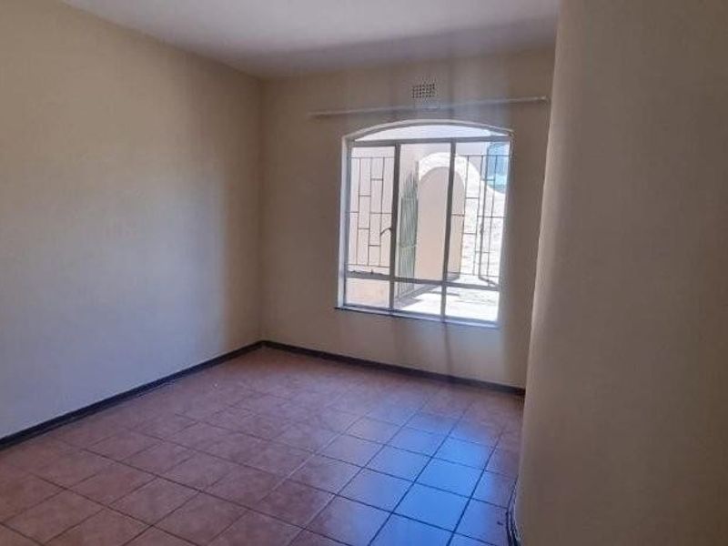 A vacant bedroom featuring tiled flooring, neutral wall paint, and a security-barred window providing natural light.