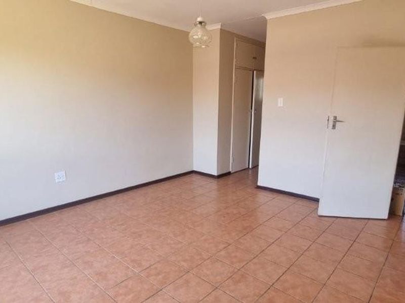 An empty living room featuring neutral wall tones, tiled flooring, and built-in storage cupboards, providing a versatile space for customization.