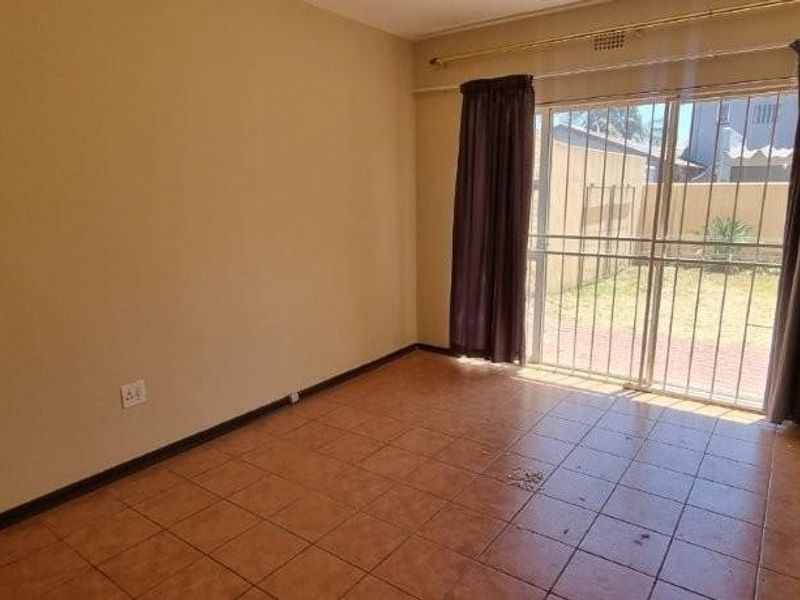 A bright, empty living room featuring ceramic floor tiles and large sliding glass doors that provide direct access to the rear garden area.
