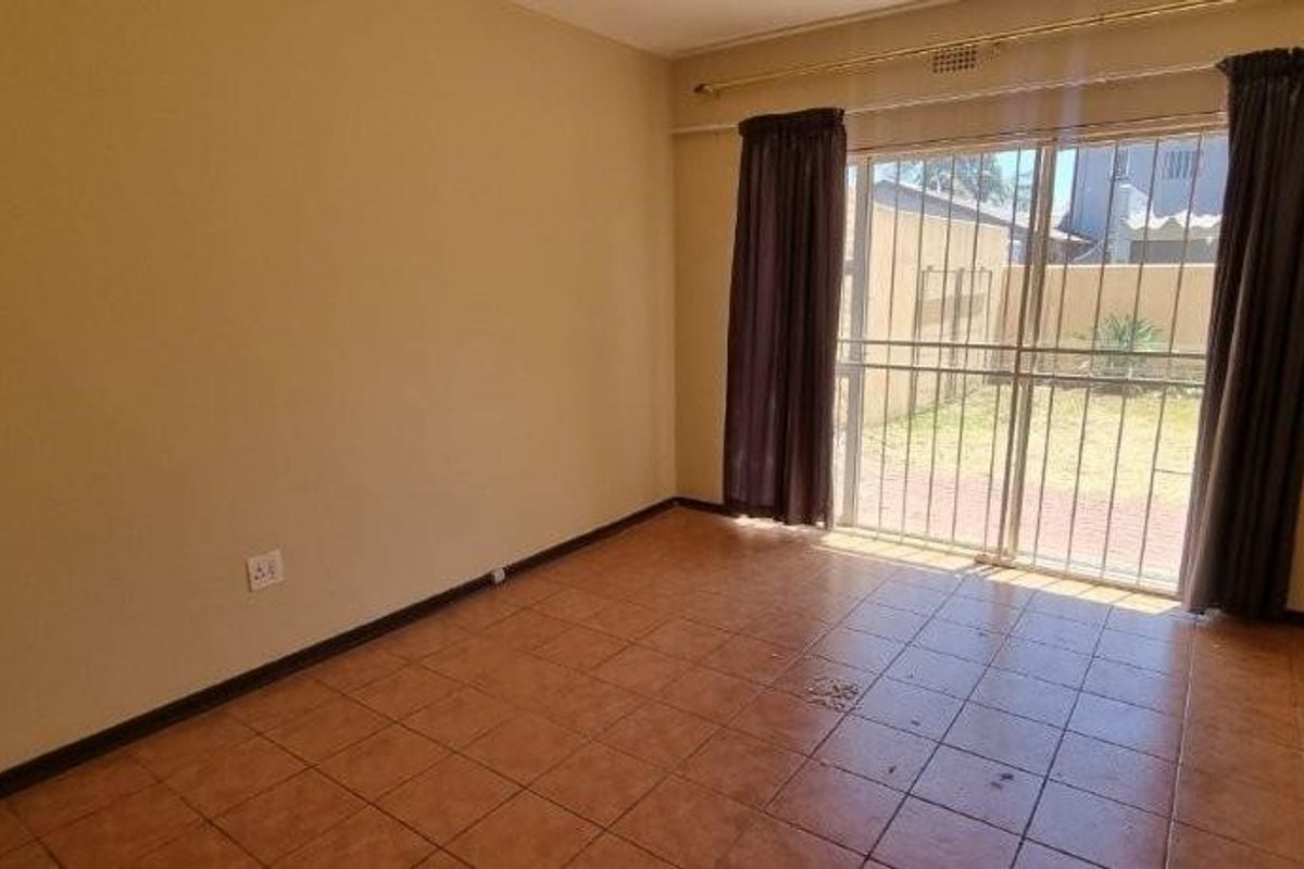A bright, empty living room featuring ceramic floor tiles and large sliding glass doors that provide direct access to the rear garden area.
