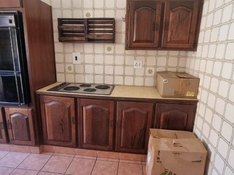 A dated kitchen featuring dark wood cabinetry, integrated double oven, and electric hob with traditional ceramic wall tiles and tiled flooring.