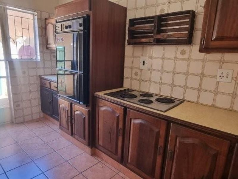 A dated kitchen featuring traditional wooden cabinetry, built-in oven, electric hob, and tiled flooring with direct access to an exterior door.