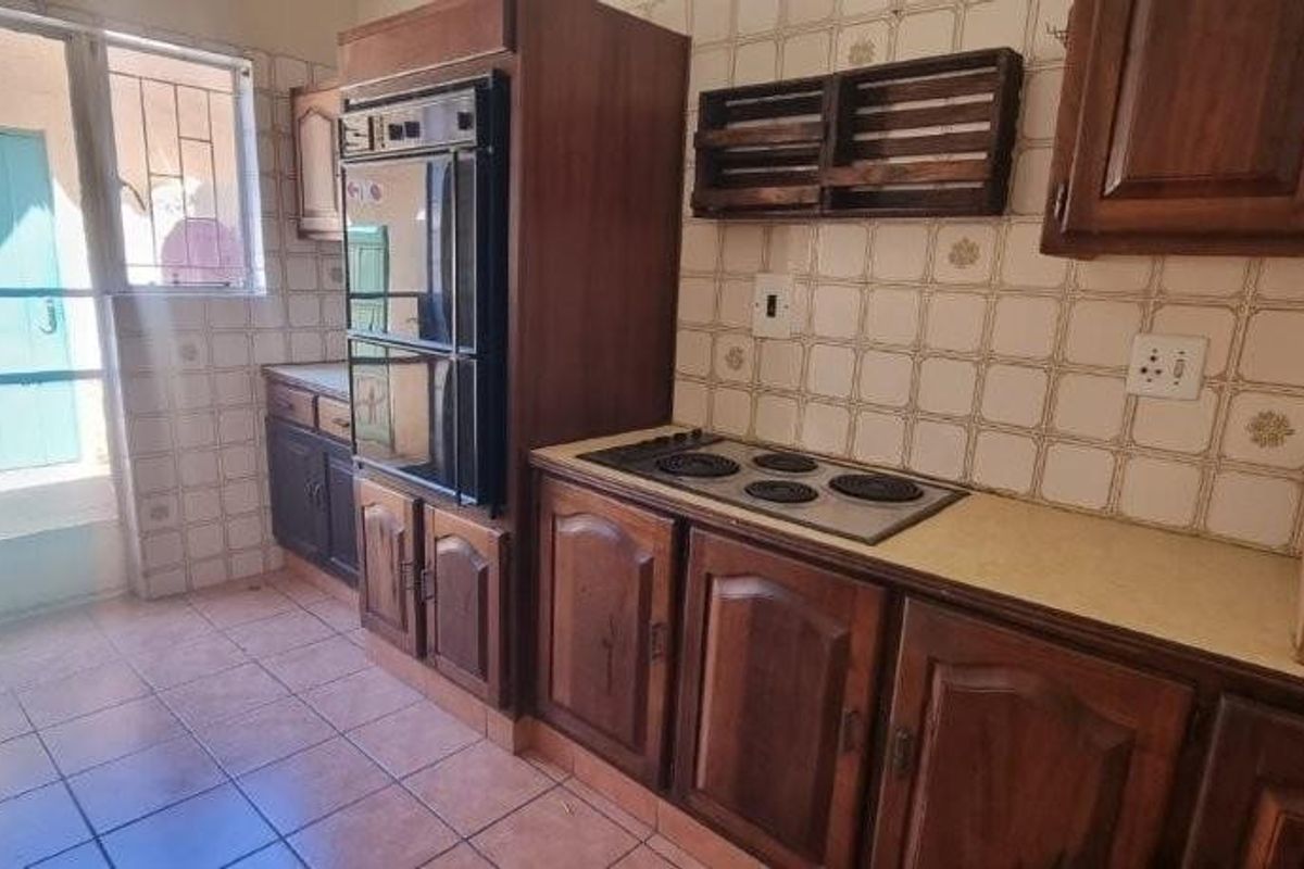 A dated kitchen featuring traditional wooden cabinetry, built-in oven, electric hob, and tiled flooring with direct access to an exterior door.