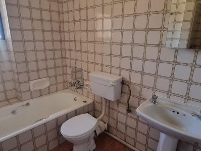 A dated bathroom featuring a standard bathtub, pedestal basin, and toilet, finished with traditional wall tiles and exposed plumbing fixtures.