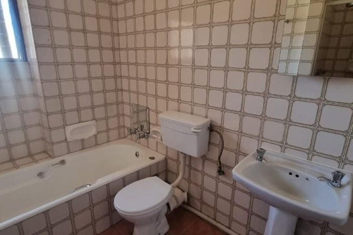 A dated bathroom featuring a standard bathtub, pedestal basin, and toilet, finished with traditional wall tiles and exposed plumbing fixtures.