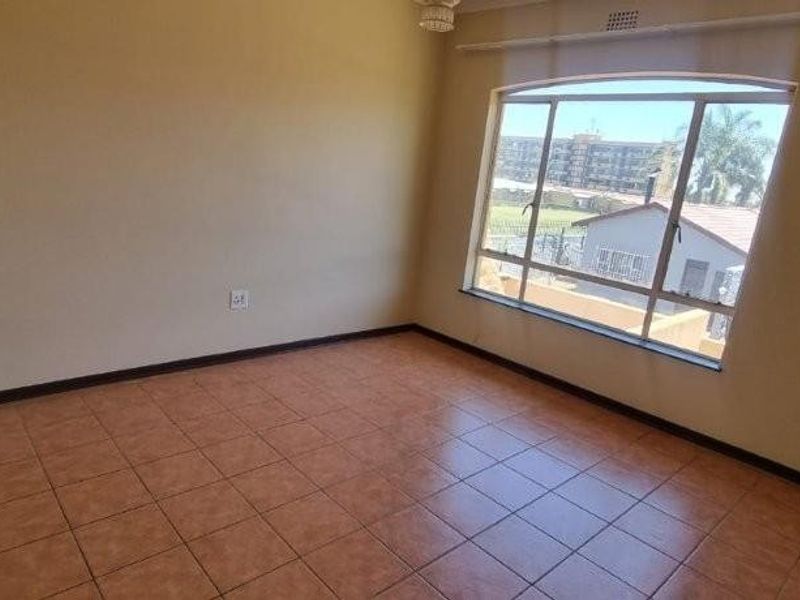 A bright, empty bedroom featuring tiled flooring, a large window with natural light, and built-in cupboard space.