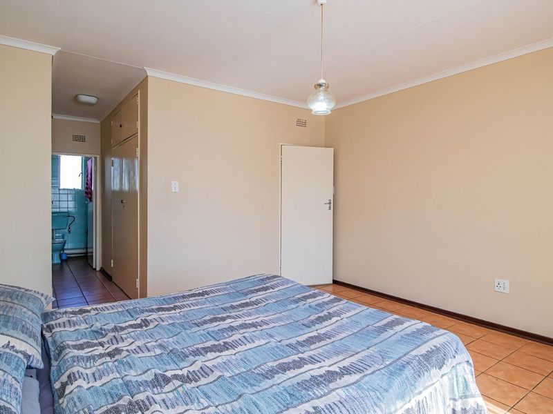 A bedroom featuring tiled flooring, built-in cupboards, and a pendant light fixture, with an adjacent view into a bathroom.