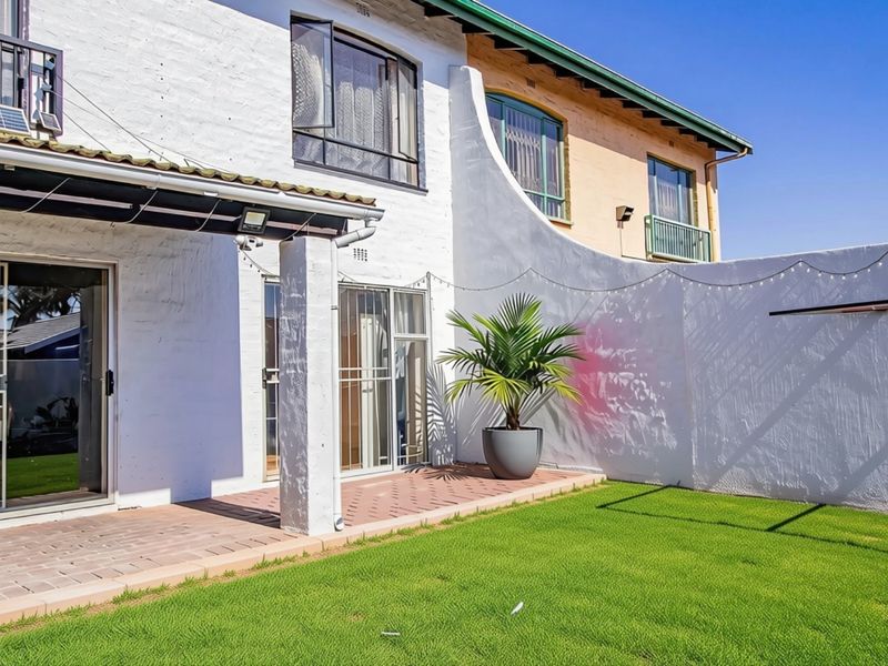 Rear view of the townhouse featuring a paved patio area, sliding glass doors with security gates, and a private lawn.