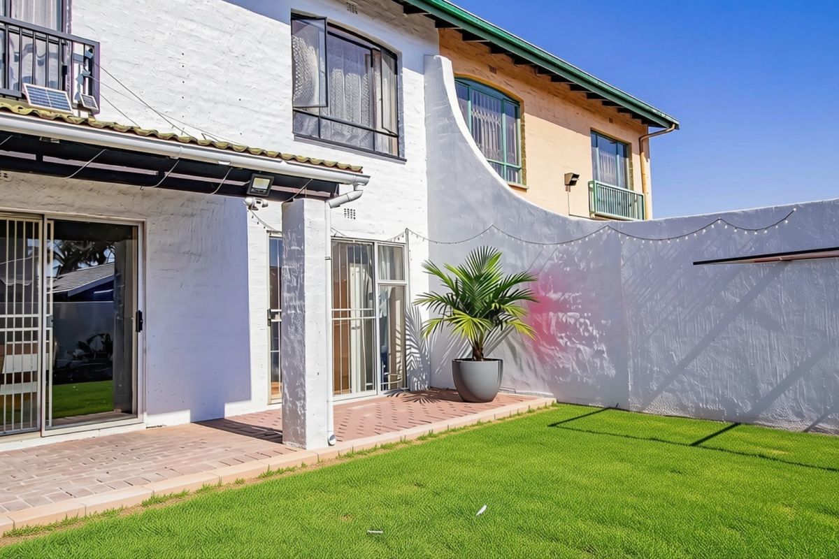 Rear view of the townhouse featuring a paved patio area, sliding glass doors with security gates, and a private lawn.