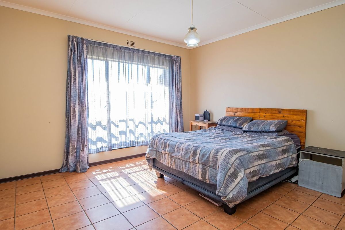A spacious bedroom featuring tiled flooring, a large window allowing natural light, and a central pendant light fixture.