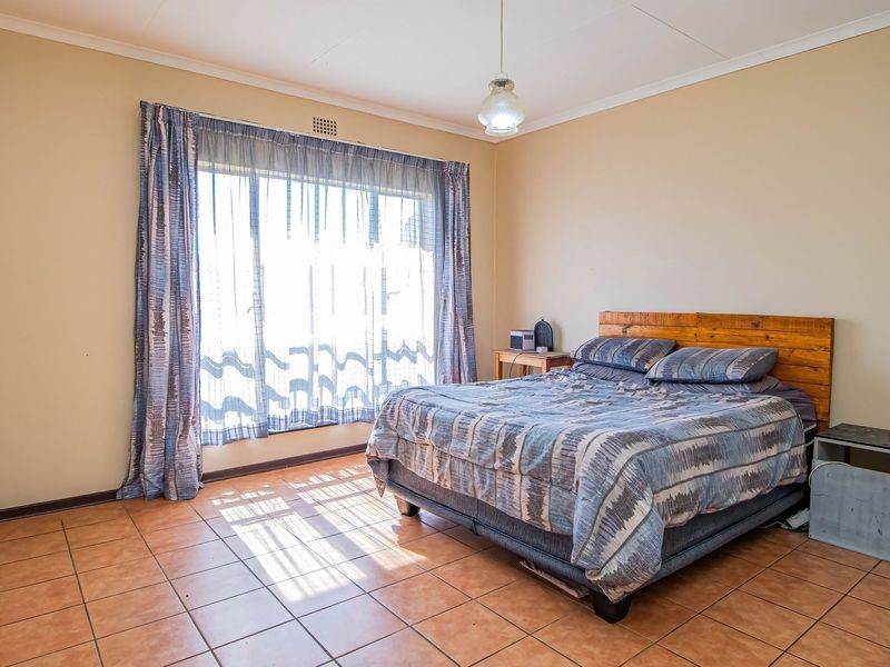 A spacious bedroom featuring tiled flooring, a large window allowing natural light, and a central pendant light fixture.