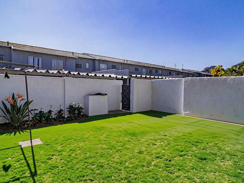 A private rear garden featuring a well-maintained artificial lawn, high boundary walls for privacy, and a built-in braai area.