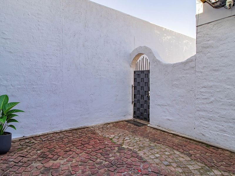 A private entrance area featuring a secure metal gate, high boundary walls, and traditional cobblestone paving.
