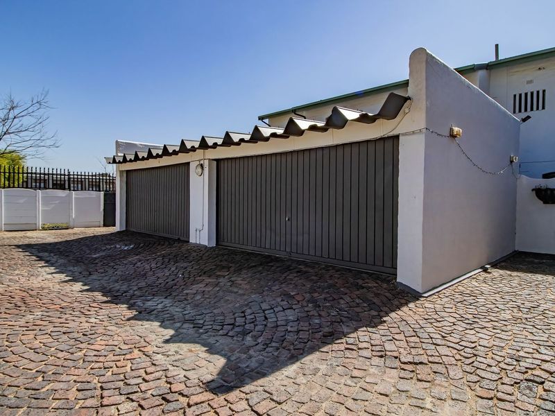 A double garage with dark grey doors and a cobblestone driveway, featuring a corrugated roof and secure perimeter fencing.
