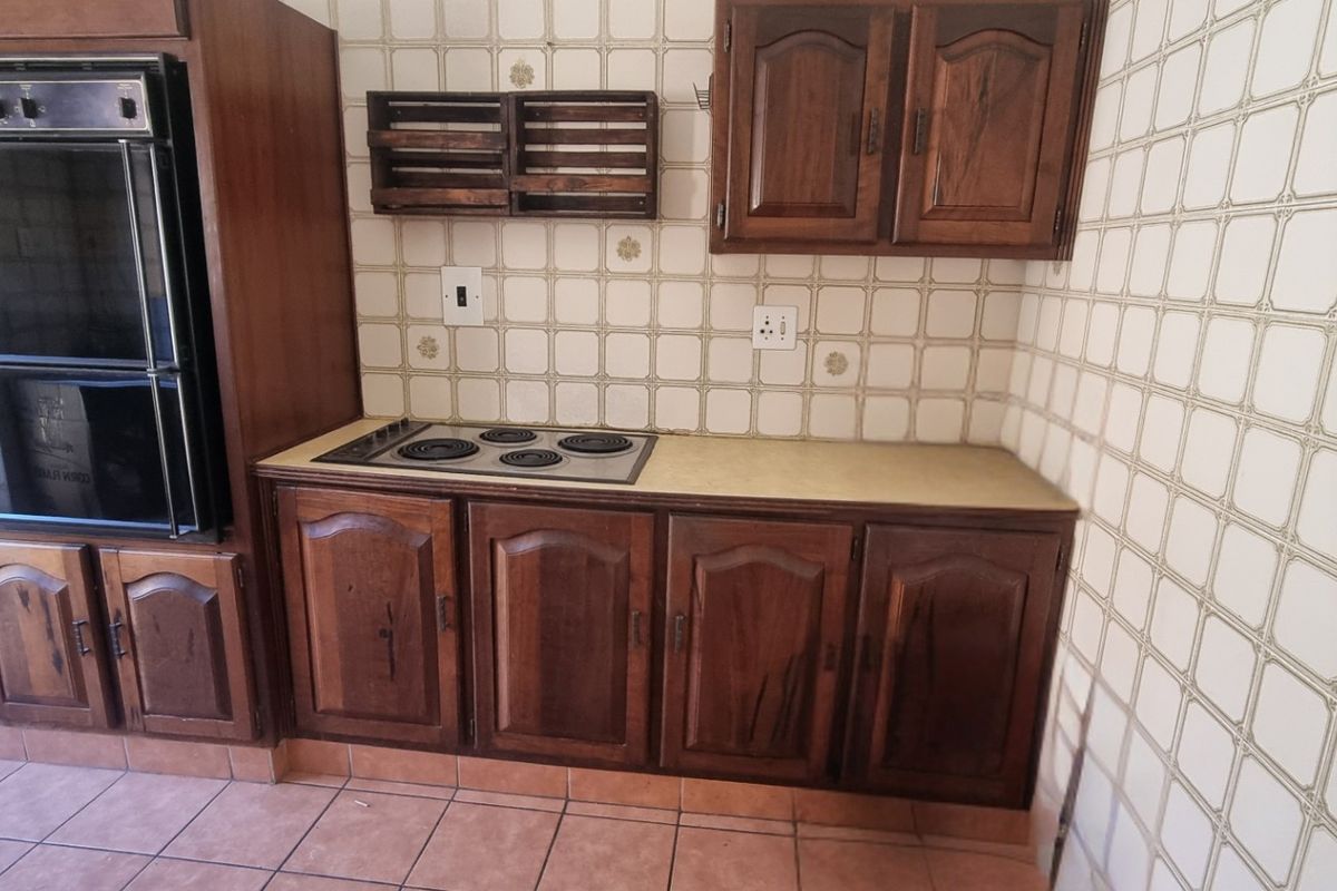 A dated kitchen featuring traditional wooden cabinetry, a built-in oven, electric hob, and tiled backsplash with terracotta-style floor tiles.