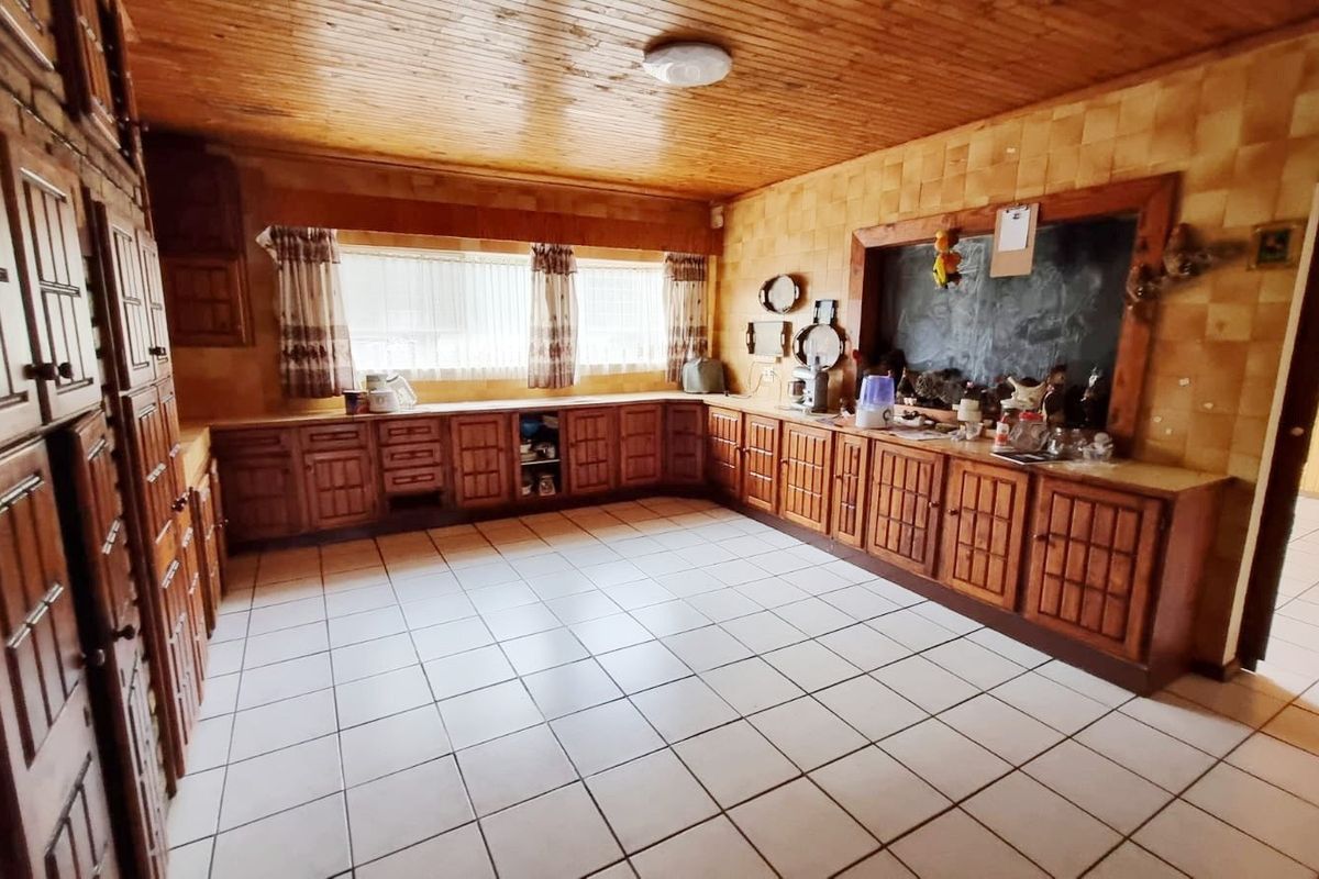 A spacious kitchen featuring extensive wooden cabinetry, tiled flooring, and a timber-paneled ceiling, offering a traditional aesthetic with significant potential for modernization.