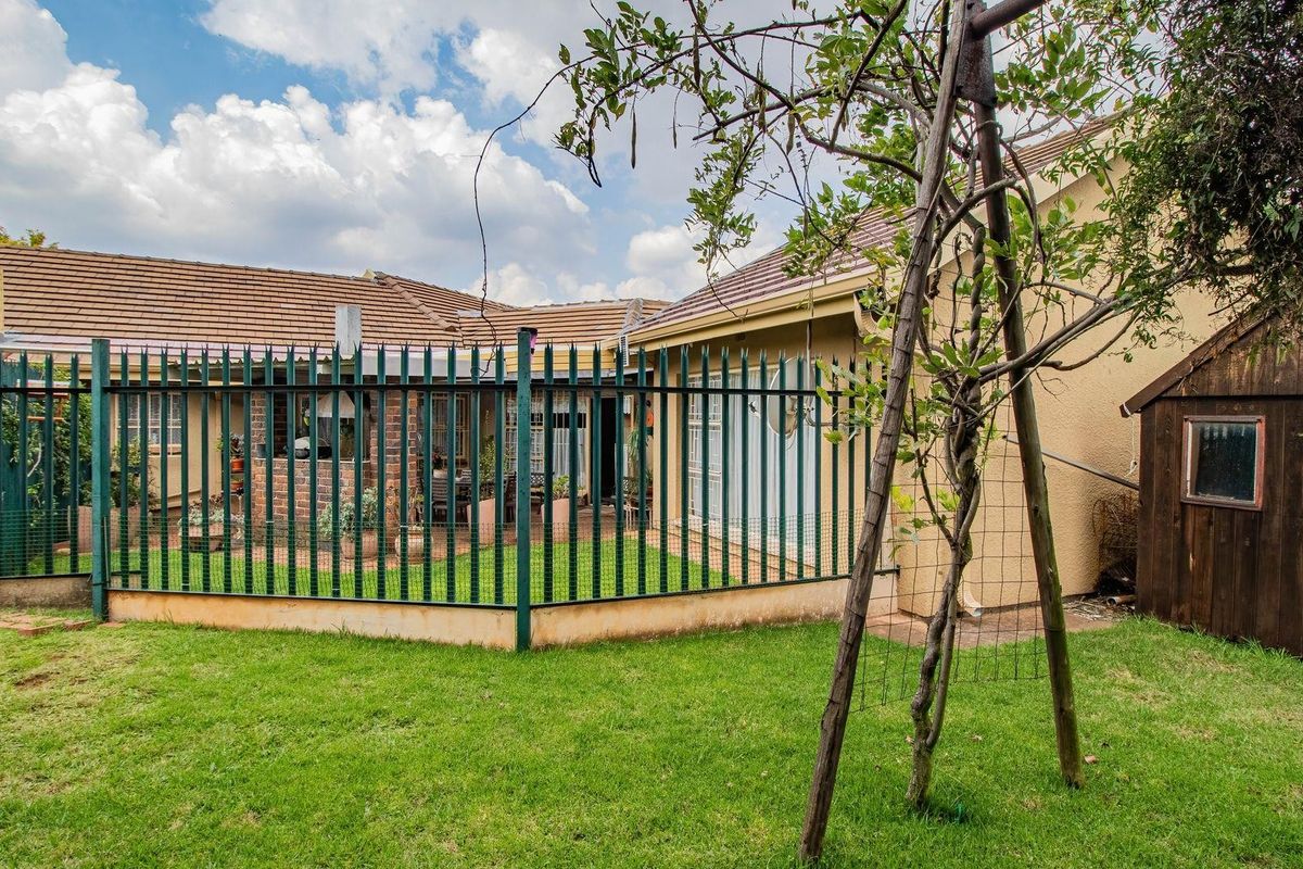 A view of the rear garden featuring a lawn, a secure fenced-off patio area, and a small wooden storage shed.