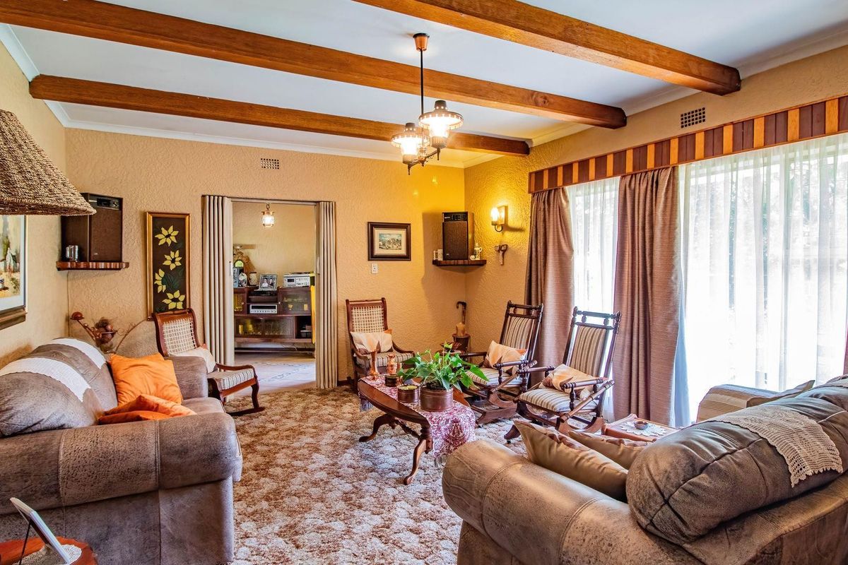 A traditional living room featuring exposed timber ceiling beams, textured walls, and large sliding glass doors providing access to the exterior.