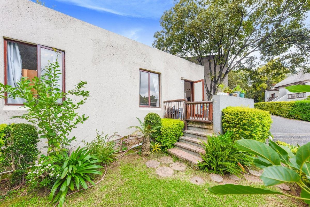 Exterior view of the townhouse featuring a small garden, brick steps leading to a raised patio area, and established landscaping.