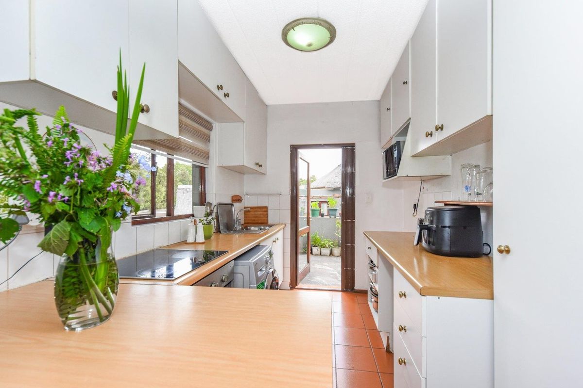 A functional galley-style kitchen featuring laminate countertops, built-in cabinetry, an integrated hob, and direct access to an outdoor patio area.