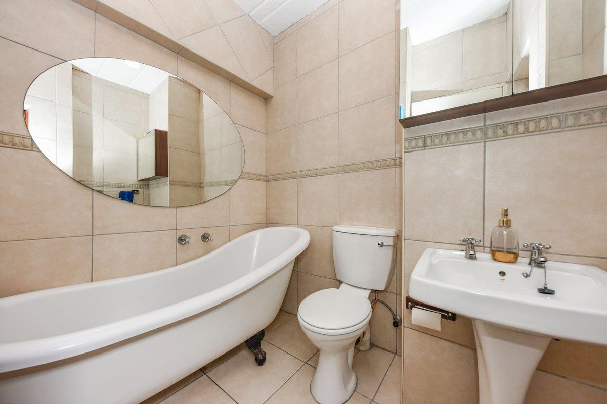 A compact bathroom featuring a classic clawfoot bathtub, pedestal basin, and toilet with neutral wall and floor tiling.