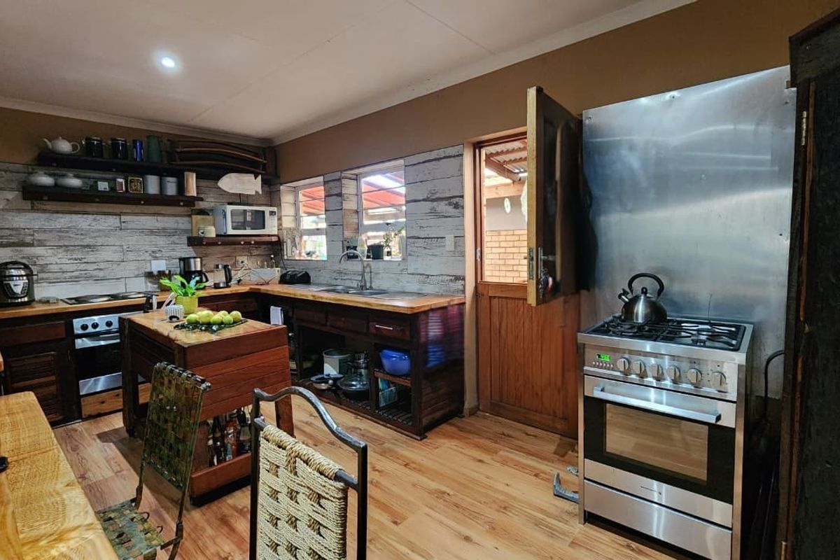 Rustic kitchen featuring wooden cabinetry, open shelving, a stainless steel gas stove, and wood-look flooring with direct access to an outdoor area.