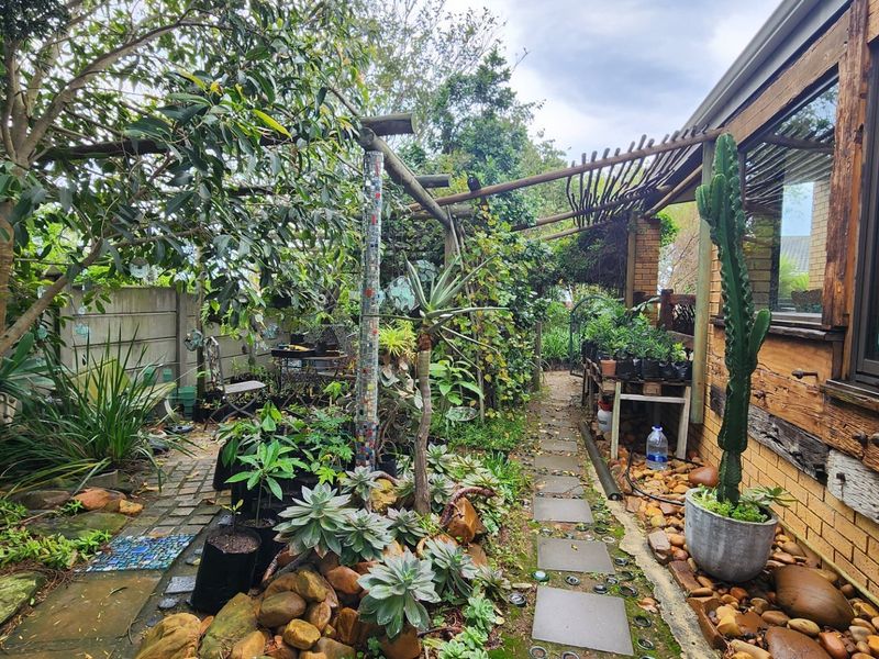 A landscaped side garden area featuring a stone paver pathway, timber pergola structure, and established garden beds adjacent to the house exterior.