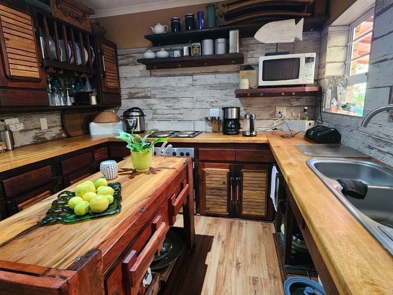 A rustic-style kitchen featuring wooden cabinetry, solid timber countertops, a double-basin stainless steel sink, and integrated shelving.