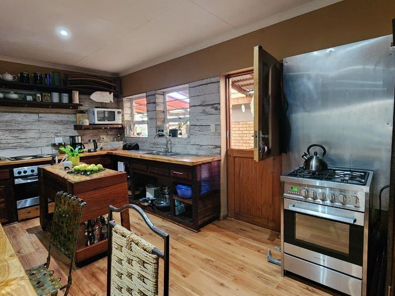Rustic kitchen featuring wooden cabinetry, open shelving, a stainless steel gas stove, and wood-look flooring with direct access to an outdoor area.