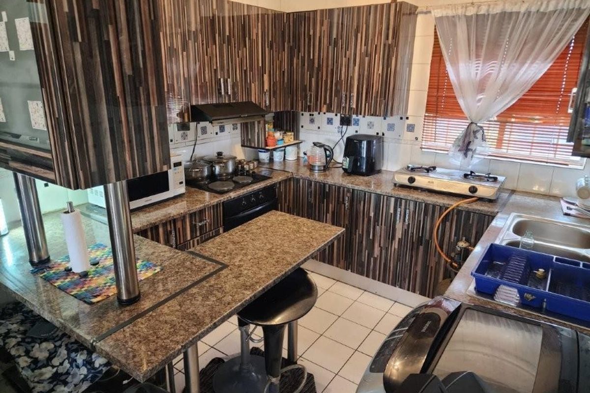 A functional kitchen featuring wood-grain cabinetry, granite-look countertops, a breakfast bar, and a tiled backsplash with integrated stove and sink fixtures.