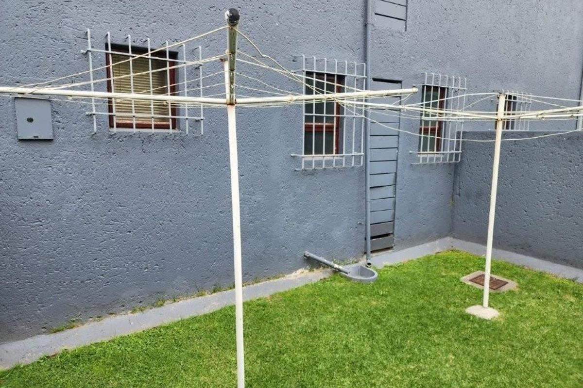 A private rear courtyard area featuring a grass lawn, exterior wall with security-barred windows, and a fixed rotary clothesline.