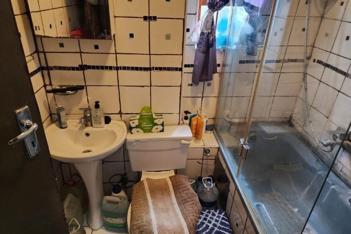 Compact bathroom featuring a pedestal basin, toilet, and a shower enclosure with glass screen, requiring significant cosmetic updates and maintenance.