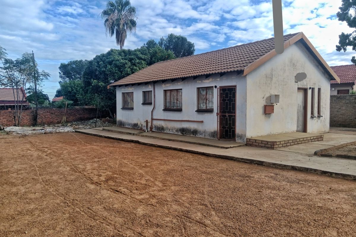 Rear view of a detached house featuring a tiled roof, security gates, and a large, unlandscaped dirt yard area.