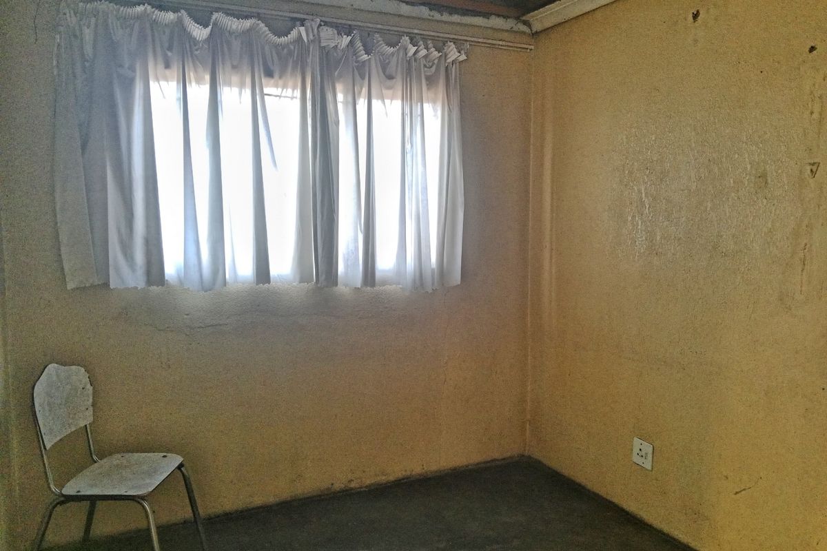 A basic bedroom space featuring exposed ceiling joists, textured yellow walls, and concrete flooring, requiring significant renovation and finishing work.