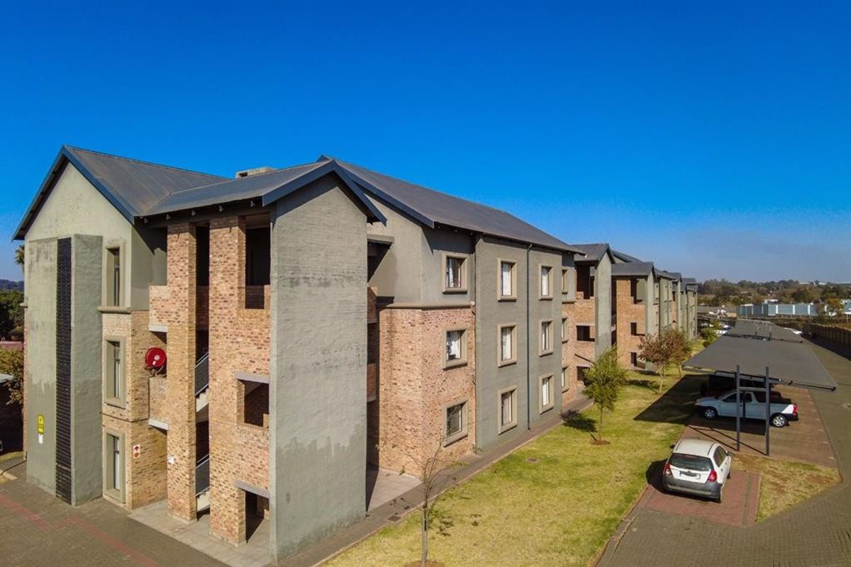 Aerial view of a multi-story apartment complex featuring brick and plaster facade, metal roofing, and dedicated covered parking bays.