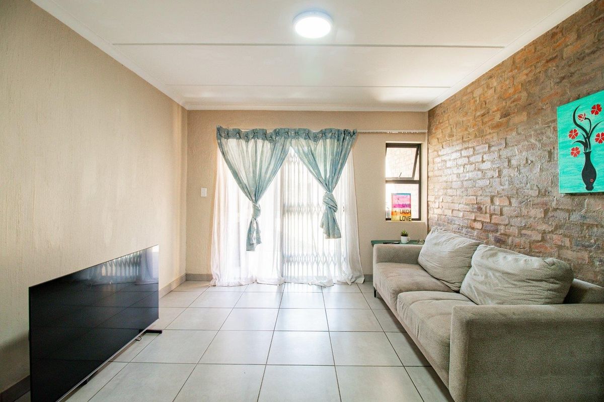 A living room featuring a prominent exposed brick feature wall, neutral floor tiles, and sliding glass doors leading to an outdoor area.