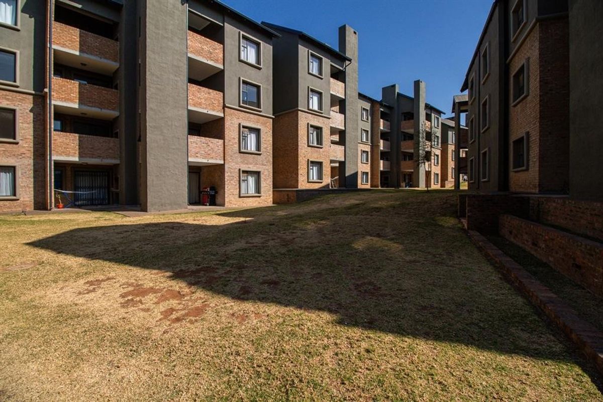 Exterior view of a modern apartment complex featuring brick and plaster facades with communal garden space between the residential blocks.