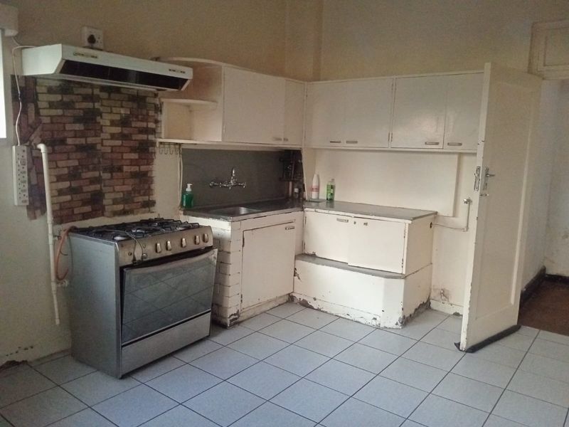 A dated kitchen featuring white cabinetry, a gas stove with extractor fan, tiled flooring, and a brick-style backsplash area.