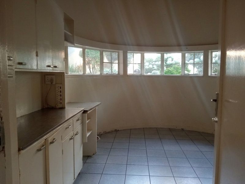 A dated kitchen area featuring curved walls, tiled flooring, and original cabinetry, offering a unique layout with natural light from a series of windows.